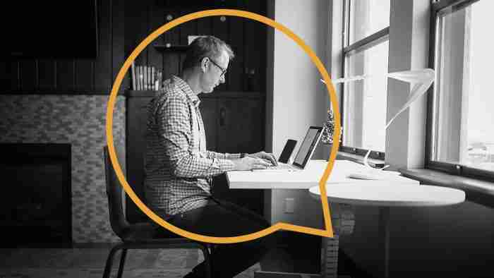 man sitting at a desk in front of the window on his laptop