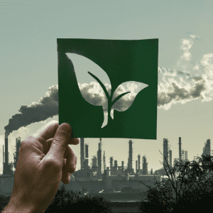 Montage of a hand holding a leaf over a picture of a power plant representing big oil's greenwashing